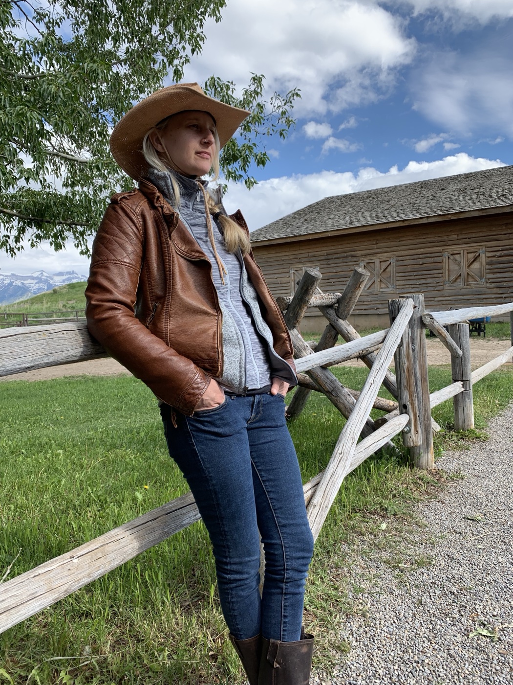 Victoria outdoors beside a rustic wooden fence, with trees and mountains behind her